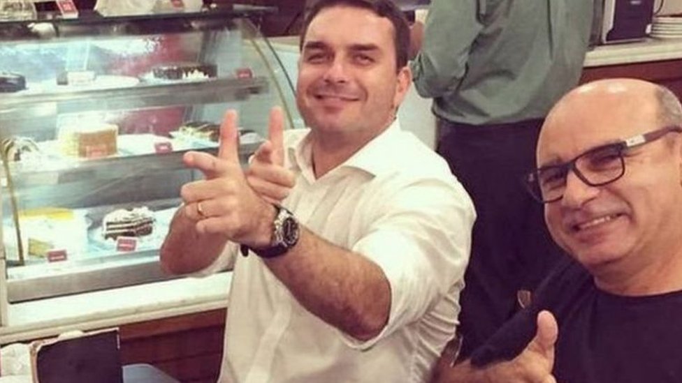 Flávio Bolsonaro e Queiroz posam para foto fazendo sinal de arma com os dedos