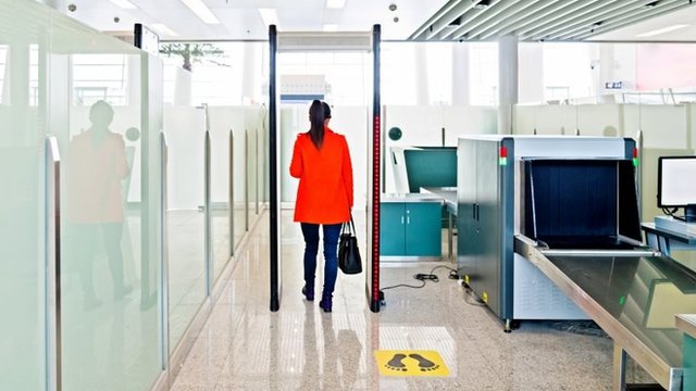 Que los agentes de aduanas encuentren sus medicamentos antirretrovirales, fácilmente reconocibles, continúa causando temor a muchos viajeros con VIH. Una mujer pasa por debajo de un arco de seguridad en el aeropuerto.