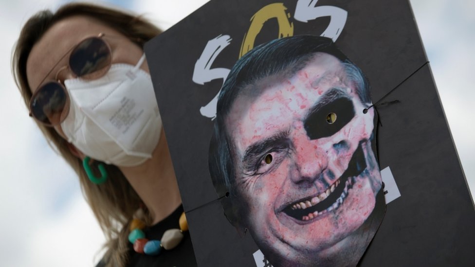 Mulher de máscara segura cartaz em que foto de Bolsonaro foi transformada em figura assustadora