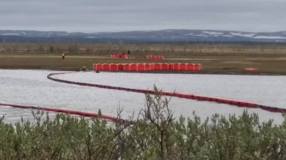 Booms across a river with water collection tanks in the background