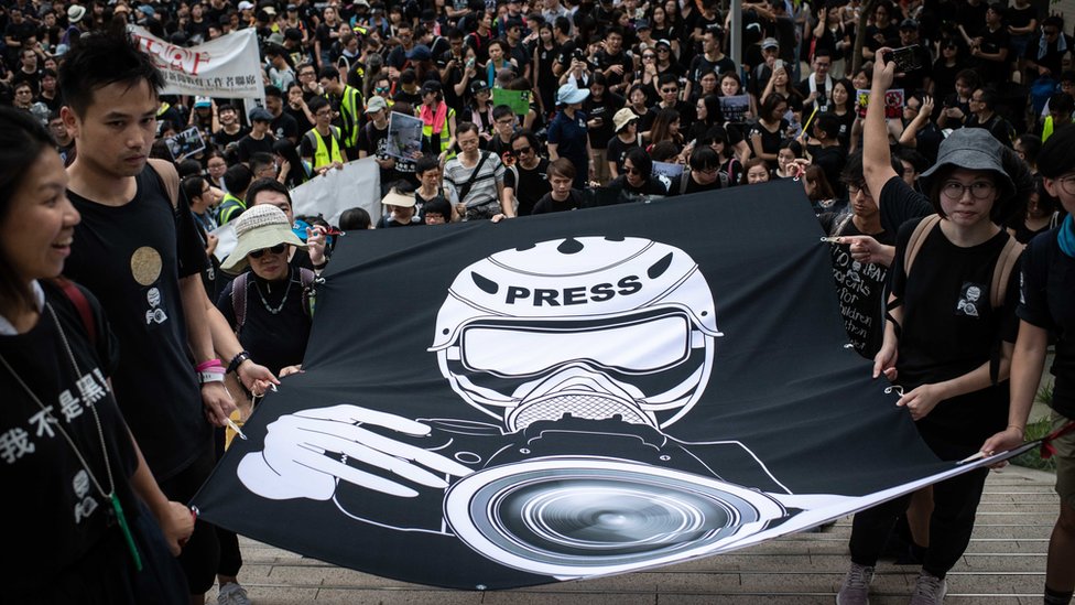 香港金鐘記者工會與支持者舉著象徵記者在示威中採訪之大型橫幅遊行抗議警察暴力對待（14/7/2019）