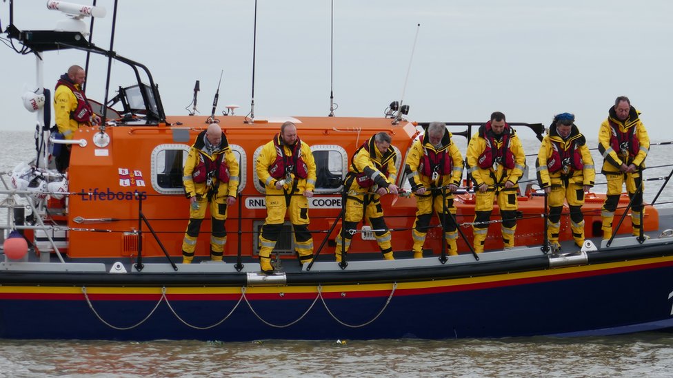 Команда спасательной шлюпки сбрасывает цветы в море