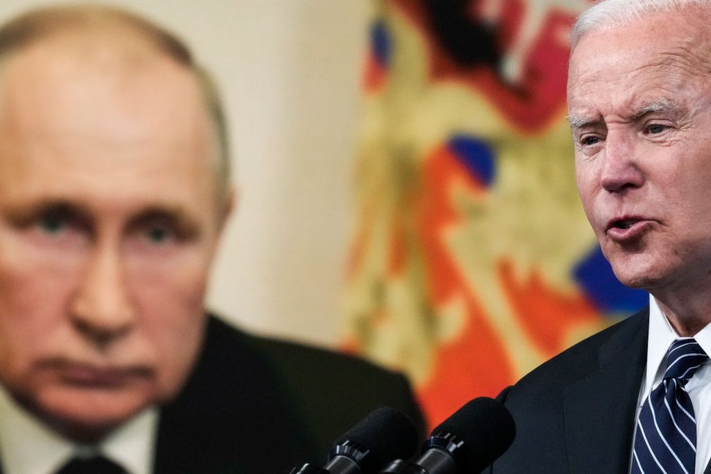 Joe Biden dando un discurso y la foto de Vladimir Putin está de fondo