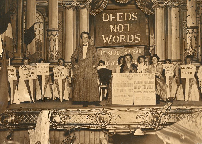 Evento da WSPU com lema da entidade ao fundo: 'ações, não palavras' ('deeds not words')