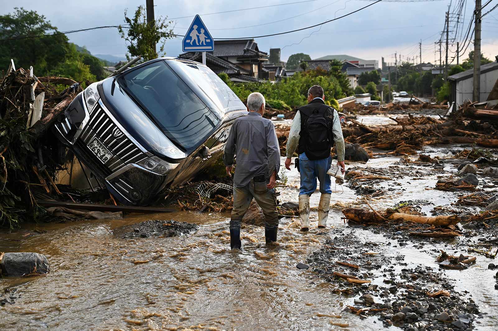 ​​Residents walk past an upturned car amid debris left behind by floods in the Japanese city of Kurume, Fukuoka prefecture - 10 July 2023