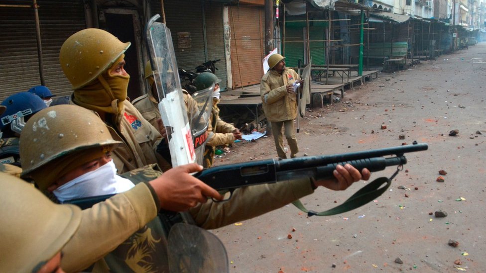 Полицейский направляет пистолет в сторону протестующих во время демонстраций против нового закона Индии о гражданстве в Канпуре 21 декабря 2019 года.