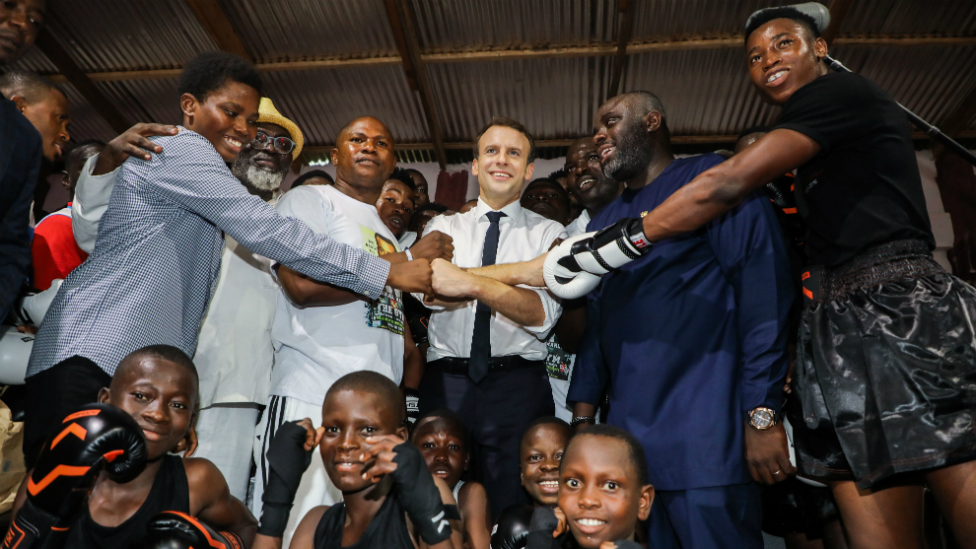 Президент Франции Эммануэль Макрон (в центре) позирует с молодыми участниками во время посещения боксерского клуба The Gym в квартале Джеймстаун в Аккре