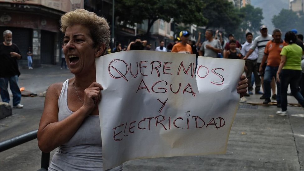 Una mujer con un cartel que dice "Queremos electricidad y agua".