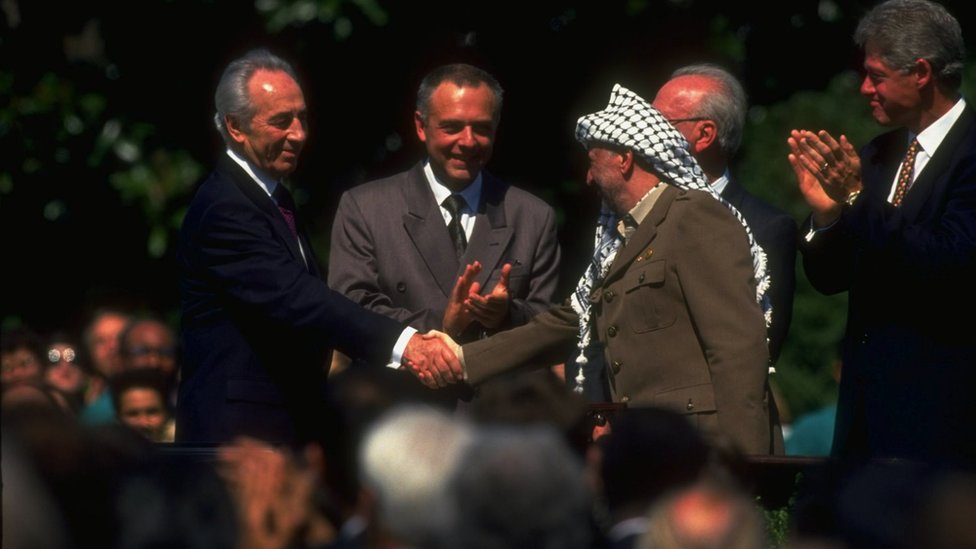 Lider PLO Jaser Arafat (desno) rukuje se sa izraelskim ministrom spoljnih poslova Šimonom Peresom na potpisivanju Sporazuma iz Osla dok američki predsednik Bil Klinton (krajnje desno) aplaudira