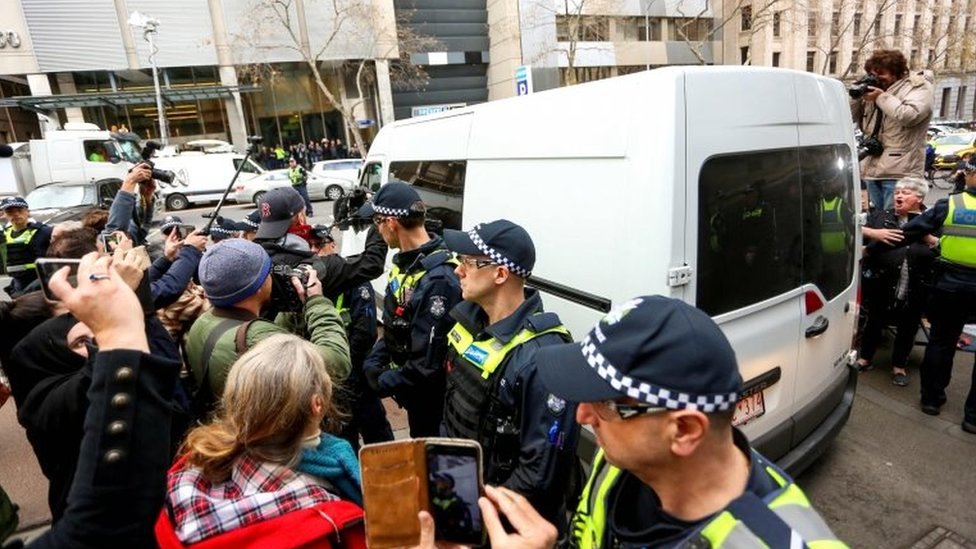 Белый фургон с Джорджем Пеллом покидает зал суда, рядом с полицейскими, представителями СМИ и представителями общественности