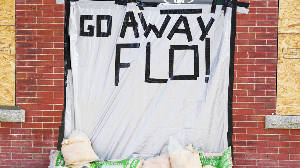 Plástico con un cartel que dice "Vete Florence", en un casa con las ventanas tapadas con paneles de madera compensada