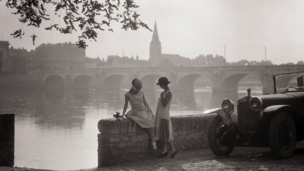 1920s TWO YOUNG WOMEN WITH ANTIQUE AUTOMOBILE SITTING STANDING TOGETHER TALKING BY STONE WALL LOIRE RIVER VALLEY FRANCE