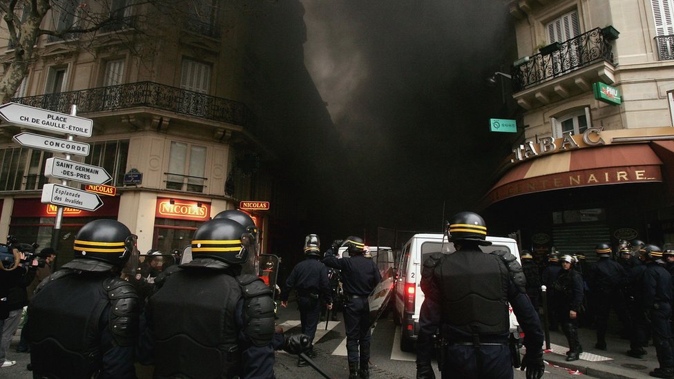 ОМОН продвигается по улице, где протестующие сожгли машины после марша против договора о найме молодежи 23 марта 2006 года на площади Инвалидов в Париже, Франция.