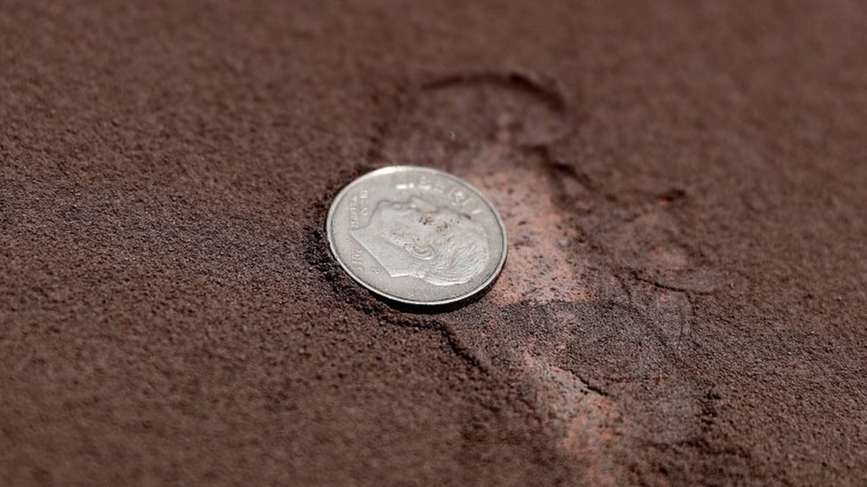 View of a coin next to the ash from the Sangay volcano on a street in Alausi, in the province of Chimborazo, Ecuador, 20 September 2020.