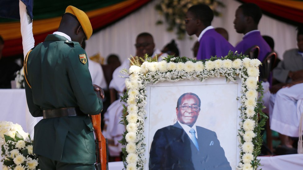 Солдат стоит рядом с фотографией бывшего президента Зимбабве Роберта Мугабе во время церковной службы в его сельской деревне в Кутаме, Зимбабве, 28 сентября 2019 г.