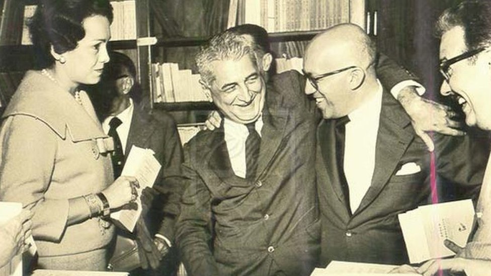 Foto em preto e branco mostra Gilberto Freyre sorrindo entre livros e amigos na Livraria São José