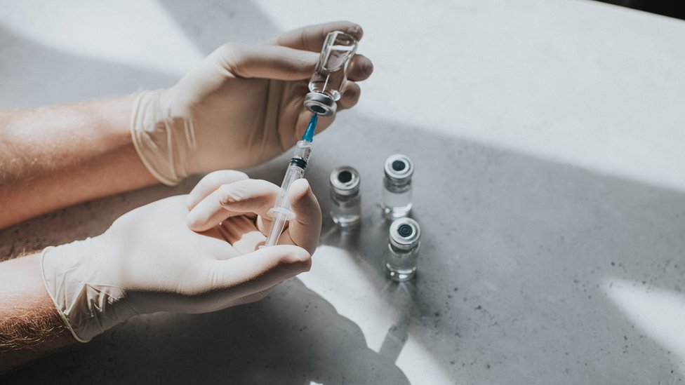 Profissional médico com luvas manuseia seringa com vacina