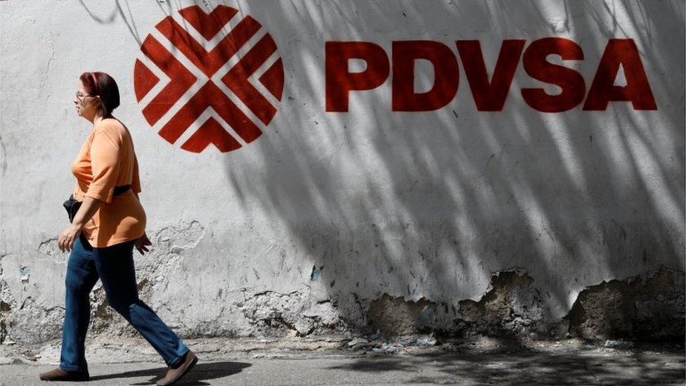 La petrolera estatal PDVSA era una de las principales fuentes de divisa para Venezuela. Una mujer camina junto a un cartel de PDVSA en Caracas.