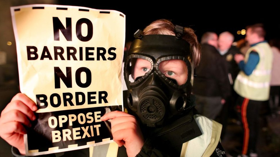 Un manifestante contrario al Brexit con una máscara de gas sujeta un cartel que dice: "sin barreras, sin frontera"
