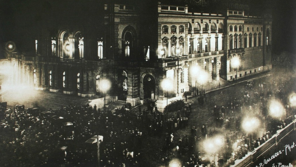 Fotografia em preto e branco da noite de inauguração do Teatro Municipal de São Paulo., com as ruas ao redor lotadas de visitantes