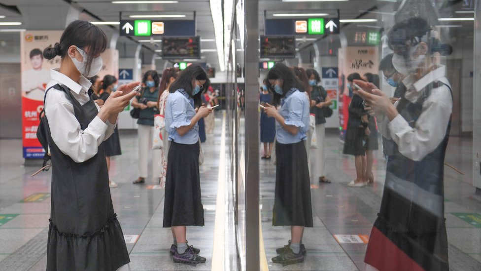 Passengers look at their smartphones as they wait for a subway train at a subway station on April 27, 2021 in Hangzhou