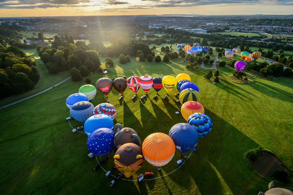 An aerial view of hot air balloons arranged in a heart shape on the ground in Bristol