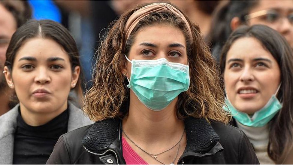 A young woman wearing a face mask is flanked by two others not doing so