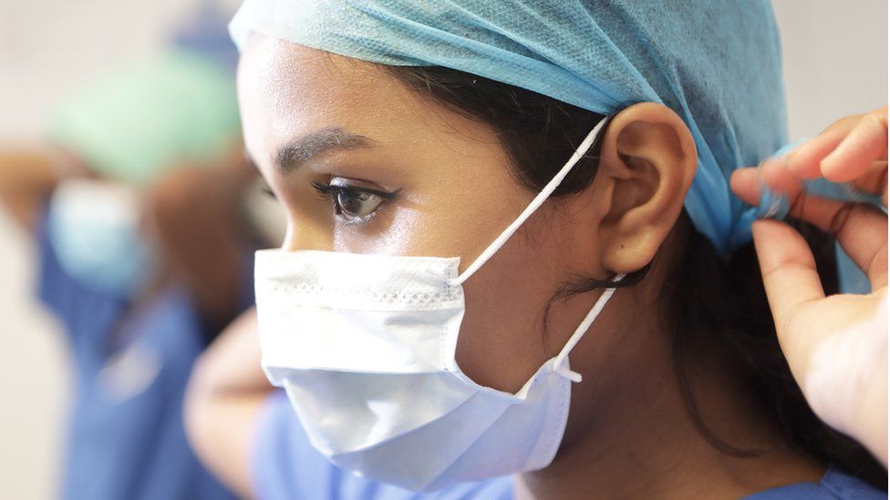 ممرضة ترتدي الكمامة وتضع غطاء الرأس في أحد المستشفيات التابعة لخدمة الصحة الوطنية في المملكة المتحدة.