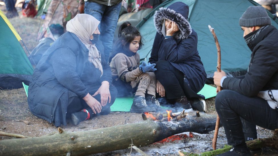 Migrantes sentados cerca de una pequeña fogata.