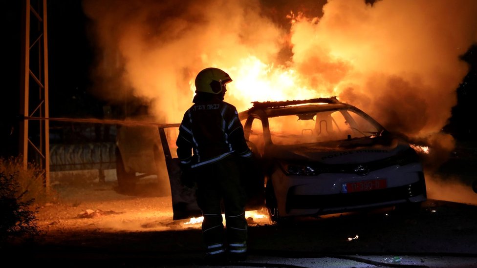 An Israeli firefighter stands near a burning Israeli police car during clashes between Israeli police and members of the country