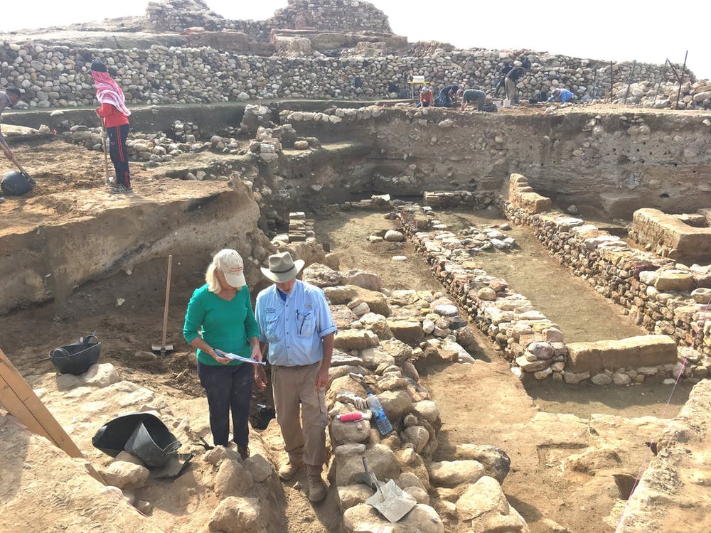 Los investigadores se paran cerca de las ruinas de muros antiguos, con la capa de destrucción a la mitad de cada muro expuesto. Phil Silvia, CC BY-ND