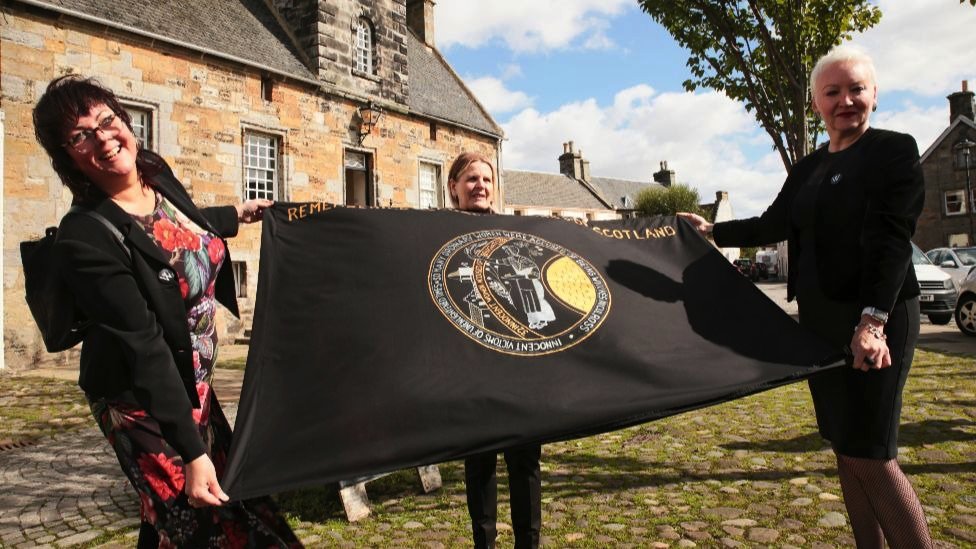 Campaigners in Culross, Scotland, holding a flag that reads, "Remembering accused witches of Scotland@