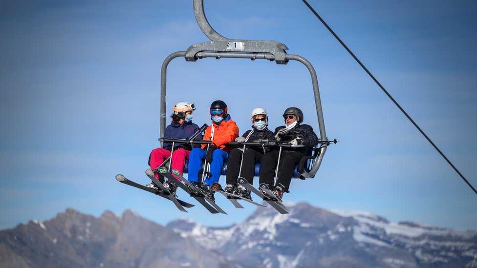 Лыжники в защитных масках для лица от распространения Covid-19, вызванного новым коронавирусом, едут на подъемнике перед спуском на склоны швейцарского горнолыжного курорта Вербье