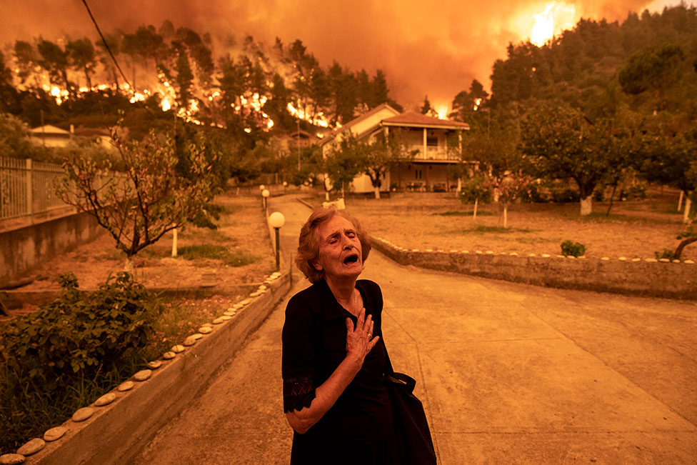 Uma idosa grita quando um incêndio se aproxima de sua casa na vila de Gouves, na ilha de Evia, Grécia, em 8 de agosto de 2021