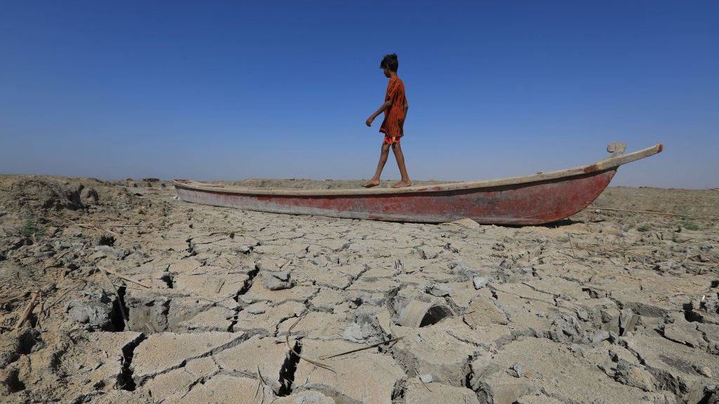伊拉克濟加爾省奇巴伊什縣一位男孩站在擱淺乾涸濕地上的小船上（28/6/2022）