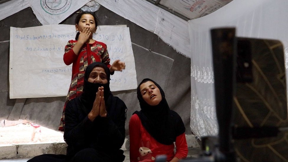 Una mujer y sus hijas jóvenes fotografiadas mientras piden donaciones en una transmisión en directo.