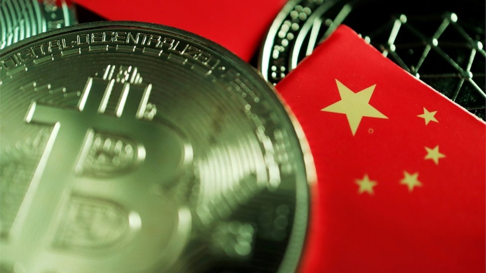 Metalna kovanica sa znakom bitkoina stoji na stolu pored malih zastava Kine