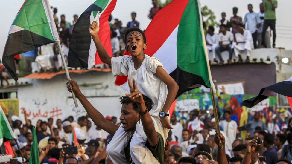 Мальчик с суданским флагом сидит на плечах мужчины среди празднующей толпы