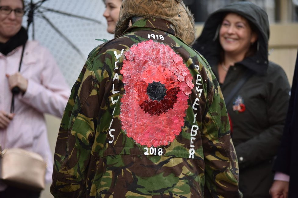 A member of the public wears a jacket with a large poppy on the back