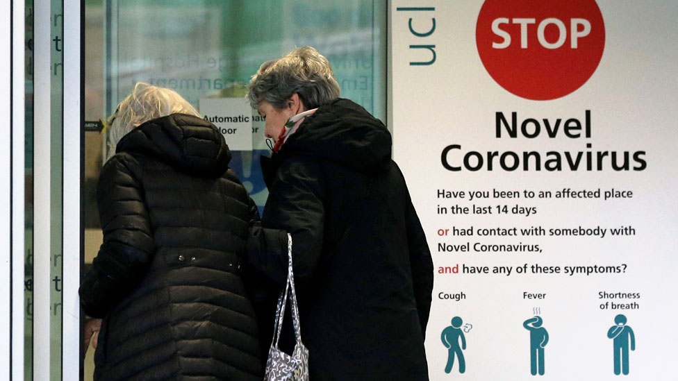 Две женщины проходят мимо указателя с инструктивной информацией о новом коронавирусе (COVID-19)
