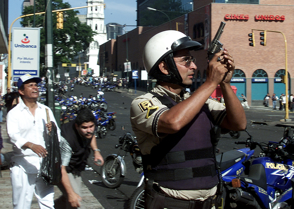 Полицейский держит пистолет во время столкновений в Каракасе 11 апреля 2002 года. По меньшей мере десять человек были убиты и более 80 ранены в результате перестрелки