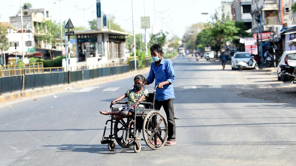 Мужчина толкает женщину в инвалидной коляске, когда они носят маски во время общенациональной блокировки, введенной правительством