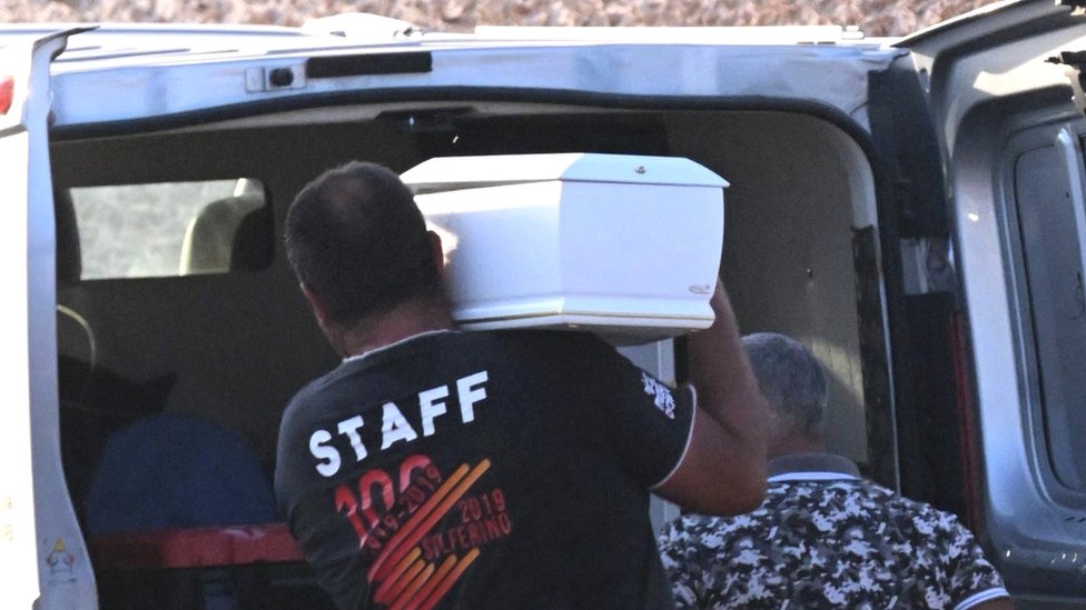 Picture of small white coffin being placed in van