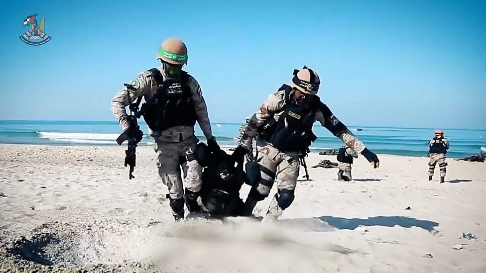訓練中，兩名身著迷彩服的男子在沙灘上拖著另一名男子