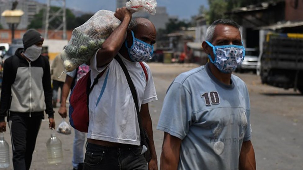 La crisis en Venezuela se vio afectada por el brote del coronavirus. Hombres en Venezuela con mascarillas y alimentos.