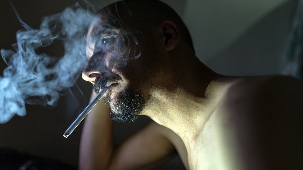Bearded man smoking, staring vacantly into the distance