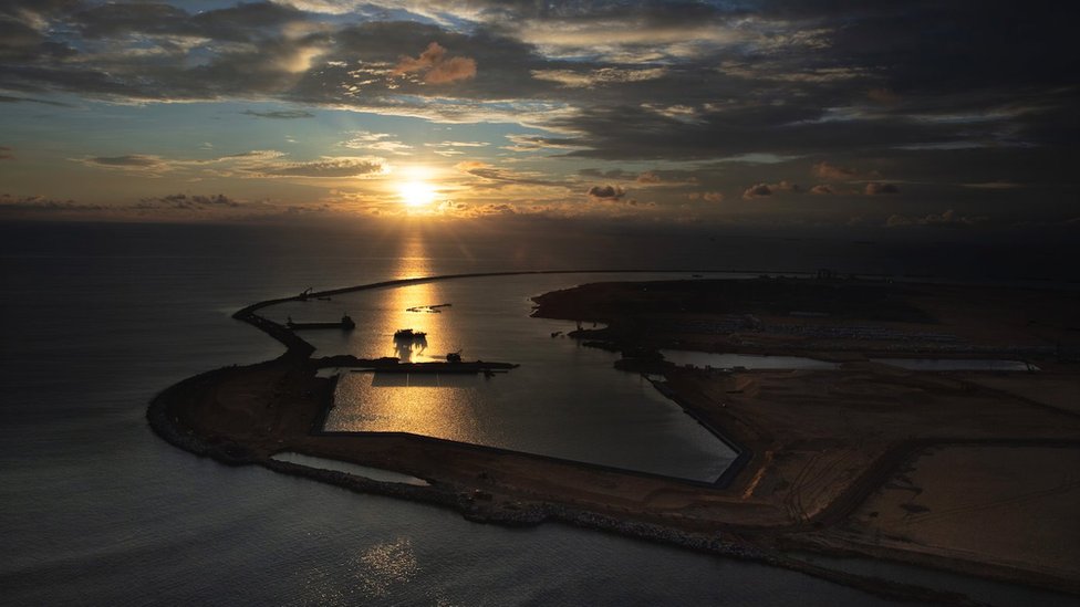 The Colombo Port City project is seen jutting out into the ocean with the sun setting over the harbour