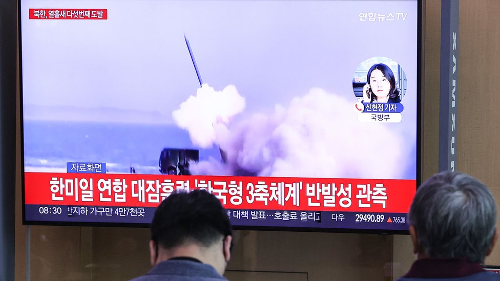 Personas viendo el lanzamiento del cohete en las noticias en televisión.