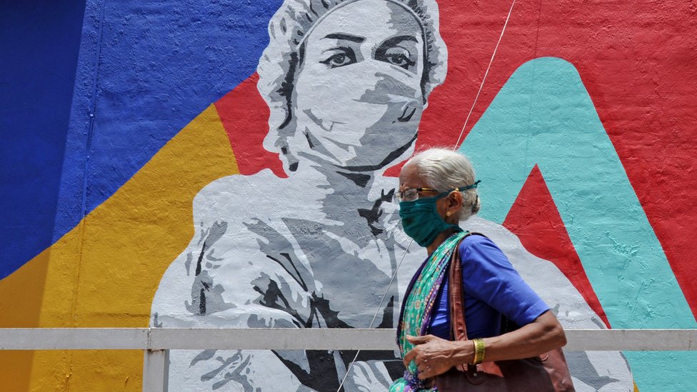 Пожилая женщина в маске проходит мимо фрески, посвященной Covid-19 в Мумбаи.