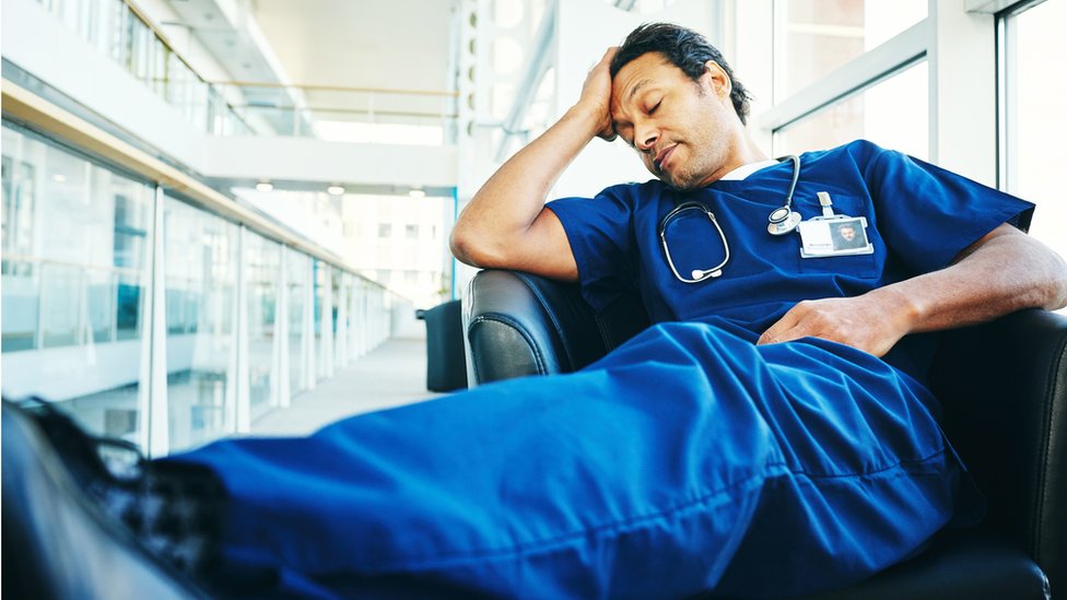 Un médico cansado duerme en un sillón de hospital.